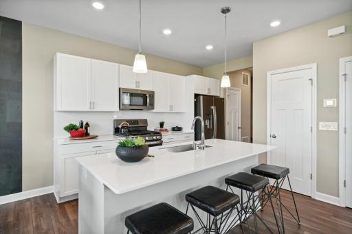 The beautiful kitchen features quartz countertops, white subway tile backsplash & pendant lighting. The island has seating for four! *Photos of model home; colors and finishes will vary.