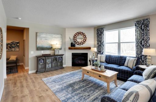 Punctuated by this corner gas fireplace, the home's main level family room is coated in hard surface flooring and is flooded in natural light via soaring windows overlooking the backyard! (Photo of model, colors may vary)