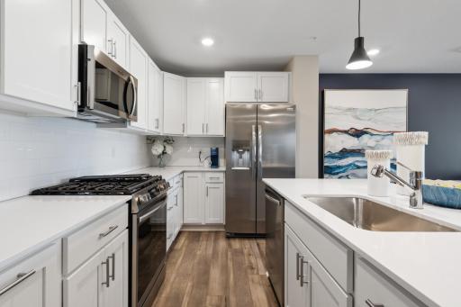 (Photo of a decorated model, actual homes finishes will vary) This spacious kitchen features quartz counters, recessed lighting, LVP wood floors, stainless appliances and more.