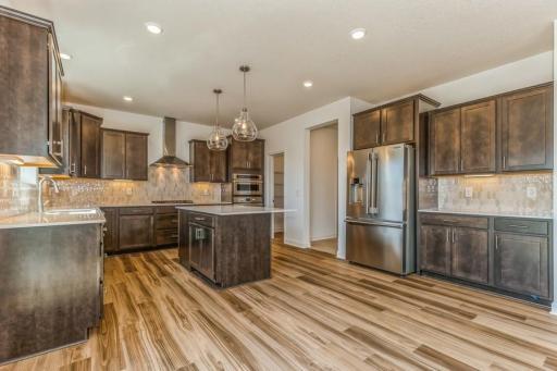 Photo is of the actual home. This spacious kitchen features a large center island, quartz countertops, recessed lighting, LVP floors, stainless appliances and more!