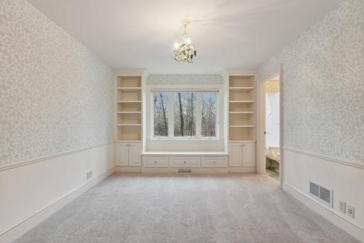 Main floor bedroom featuring a window bench flanked with built-in cabinetry, a walk-in closet and private full bath