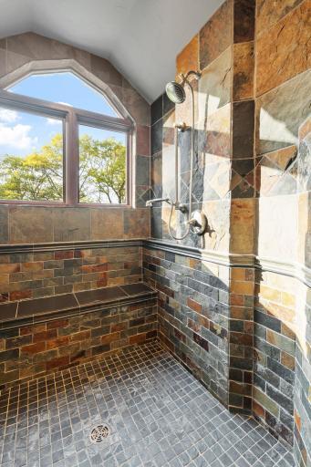 Custom walk-in shower features dual shower heads, handshower, bench and full slate tile surround