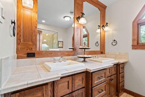 3/4 bathroom features custom oak vanity cabinet with tile top and wide spread faucets and built-in oak framed mirror with decorative sconces