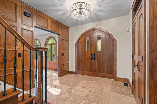 Entry offers two story oak paneled accent wall, travertine stone tile flooring and generous size coat closet boasts automatic light and French doors w/ transom window