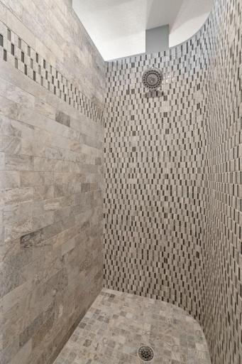Custom walk-in shower with curved wall and offers a travertine subway and mosaic tile surround