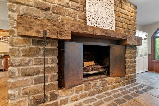 Oversized wood burning fireplace with forged steel doors, stone surround and hand hewn barn beam mantle