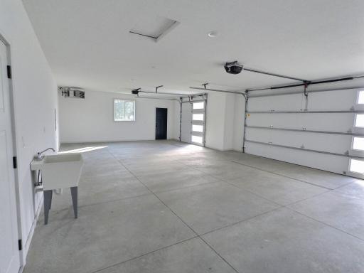 Interior of the oversized 3 car garage, floor drains by both doors, laundry sink and access to the mechanical room. Garage heater that is controlled by a thermostat to set as you please.