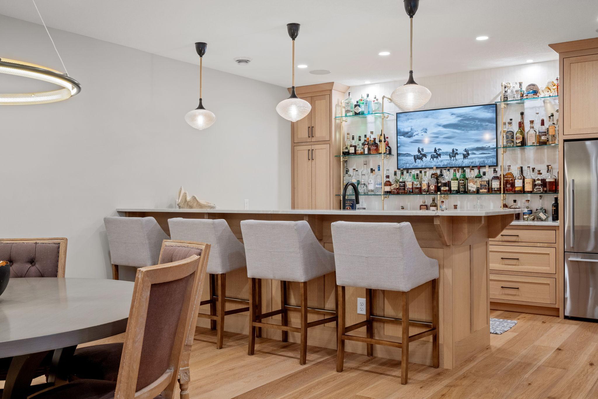 The bar area in the lower level features quartzite counters, a Bosch dishwasher, a wine fridge, and a full-size counter-depth refrigerator.