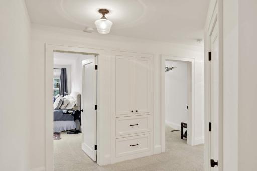 The hallway leading from the primary and second bedroom features a large walk in linen closet (on right) and another built in combination cabinet and drawers.