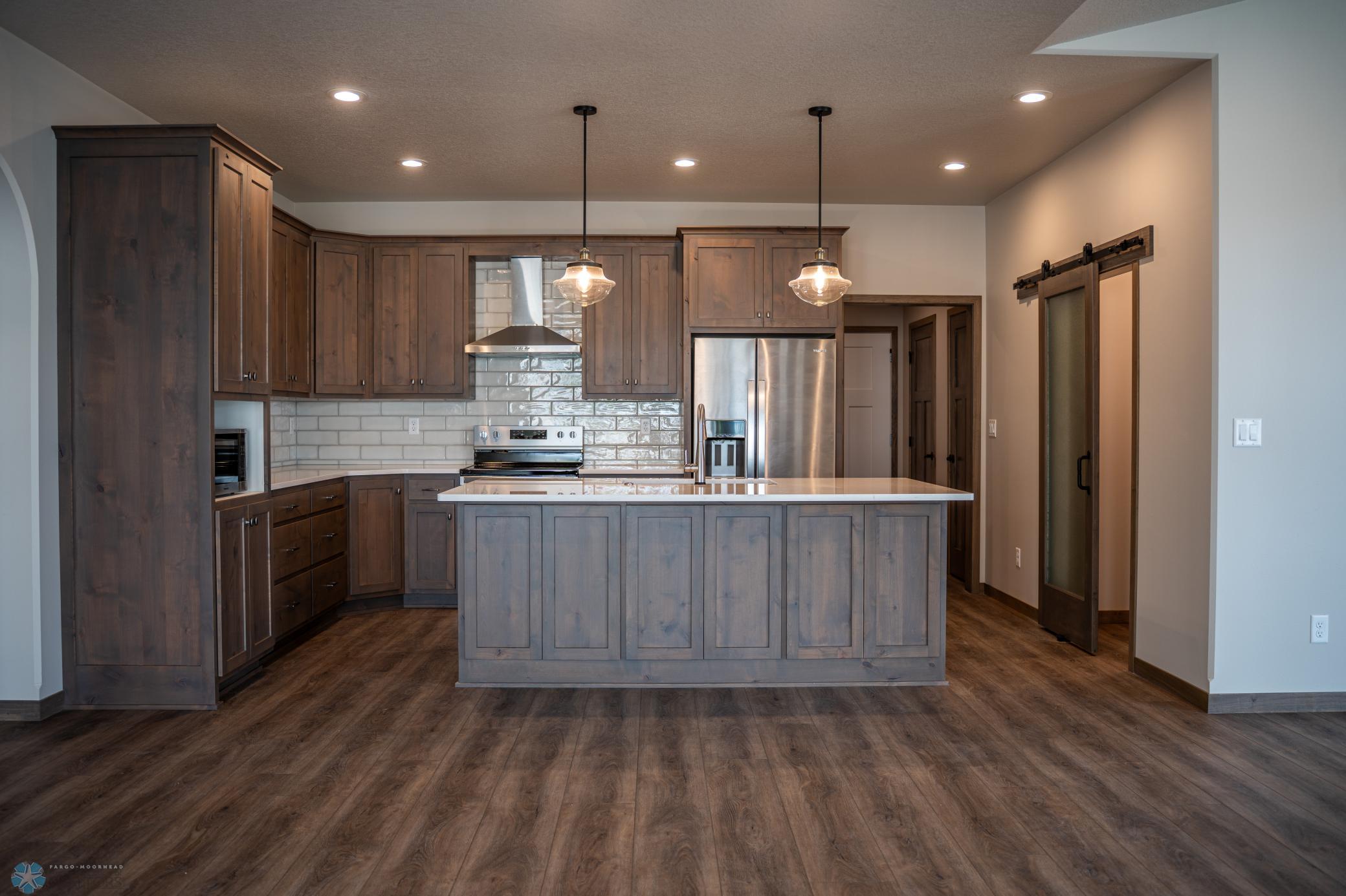 Kitchen with island, quartz counter tops, tile backsplash, stainless steel appliances, exhaust hood and walk in pantry.