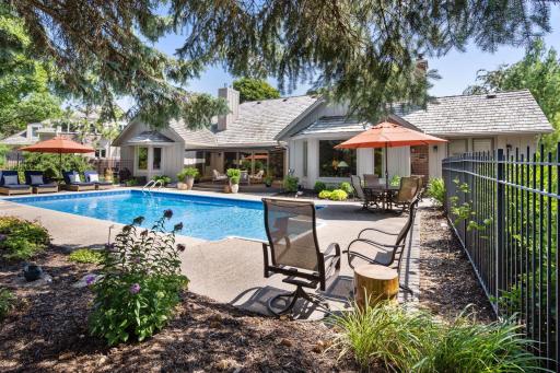 Fully fenced pool area with lush landscaping and multiple seating areas