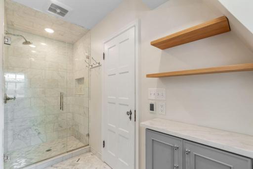 Custom shower features full marble tile surround, shampoo niche and frameless glass enclosure
