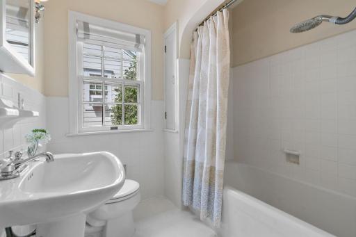 Upper level Full Bathroom features a tub w/ tile surround and original arched opening, tile wainscoting, built-in linen closet, charming pedestal sink and a pair of sconces