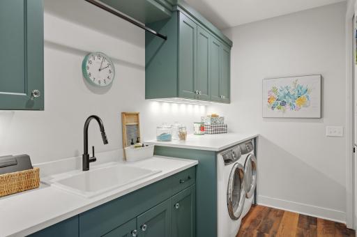 The main-level laundry room is equipped with stunning forest green cabinetry, Electrolux front load washer and dryer, and a utility sink.