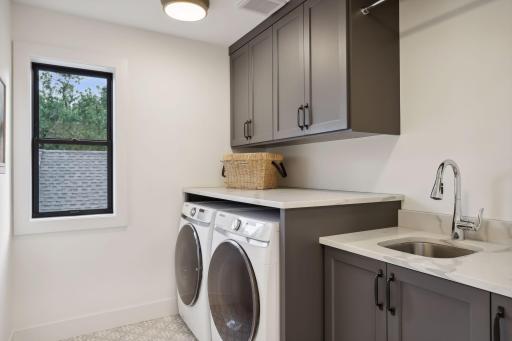 Second level laundry room with heated floors, deep sink, quartz countertops, and custom cabinets.