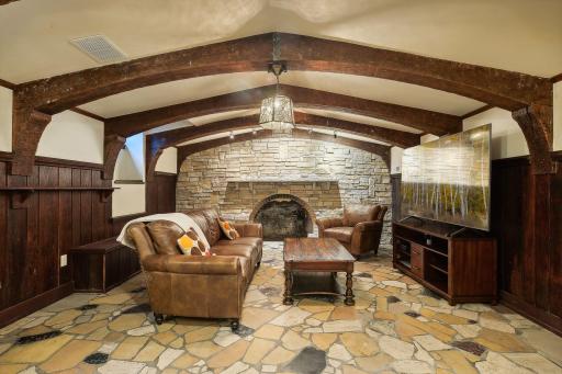 Cozy old world pub room/media room with decorative fireplace, wood beamed ceilings and paneling, and wet bar.