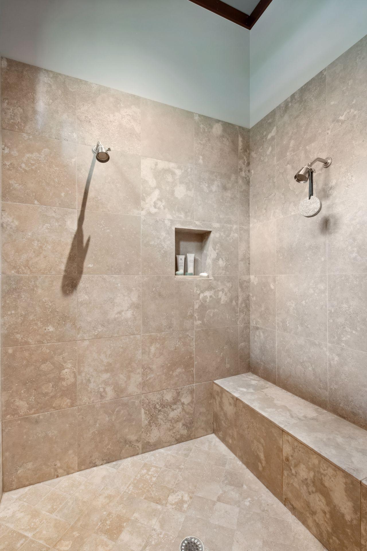 Dual shower heads and sitting ledge in primary shower.