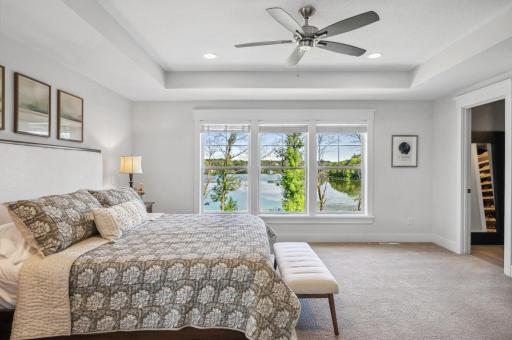 Retreat to the upper level, where the primary suite is a true sanctuary. The bedroom features a tray ceiling and a wall of windows that frame the stunning lake views.