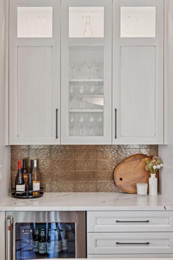 Elevate your entertaining with this wine bar, featuring a wine fridge and beautifully lit, glass-front cabinets to showcase your fine stemware!
