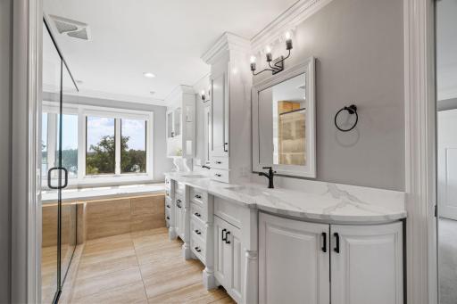 Large enameled vanity cabinet and linen tower with quartz top. Pair of decorative storage cabinets with glass doors and modern tile flooring that offers in-floor radiant heat