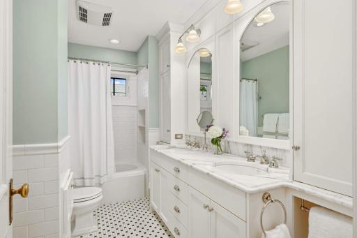A gorgeous full bath with a double vanity, Carrara marble countertops, white subway tile walls, and classic black and white floor tile