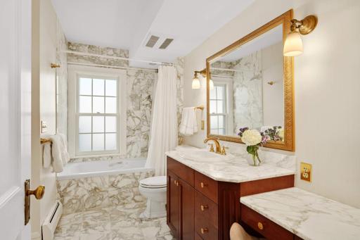 Full primary bath with rare Italian Calacatta Gold marble floors and countertops, a cherry wood vanity and a jetted bathtub.
