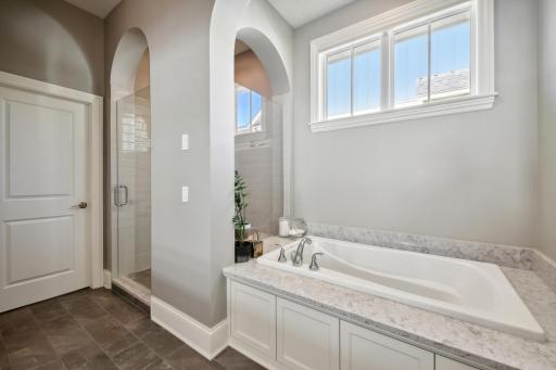 A soaking tub with granite surround and shower with subway tile surround