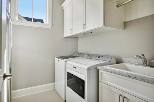 Main floor Laundry room with upper cabinets, a clothes rack and sink with pullout drawers in cabinet.