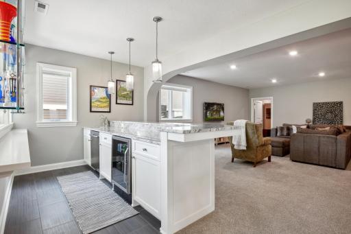 The wet Bar features a dishwasher and wine refrigerator, granite countertops, pullout shelves and floating tempered glass shelving.