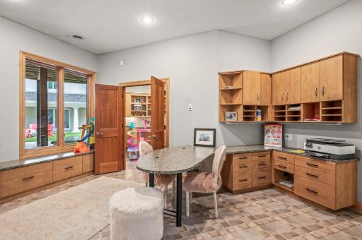 A spacious playroom is connected to a craft room, offering abundant built-in cabinets and desks for creative activities, making it a versatile space for all ages.