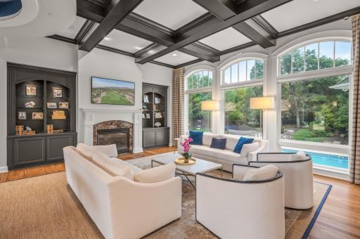 The family room is a masterpiece, featuring striking coffered black ceilings that contrast beautifully with the cozy gas-burning fireplace. Built-in shelving adds both style and functionality to the space.