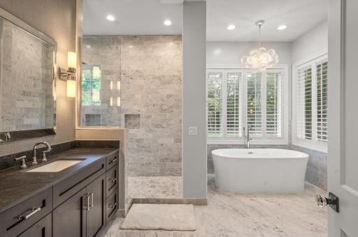 The primary bath is a spa-like oasis, featuring dual vanities, in-floor heating for added comfort, a generously sized soaking tub for relaxation, and a walk-in shower stall with sleek design.