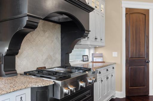 Gas range, stone counters, brick backsplash & intricate hood vent customize the space