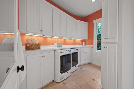 Main level laundry room is equipped with a brand-new washer and dryer (2022), tons of cabinetry, and a utility sink.