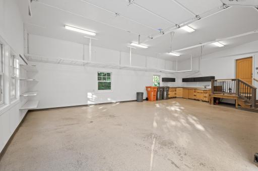 Spacious 4-car garage setup with an oversized 2-car heated garage featuring freshly painted walls, sleek epoxy floors, EV charging port, built-in cabinets, floor drains, and a utility sink.