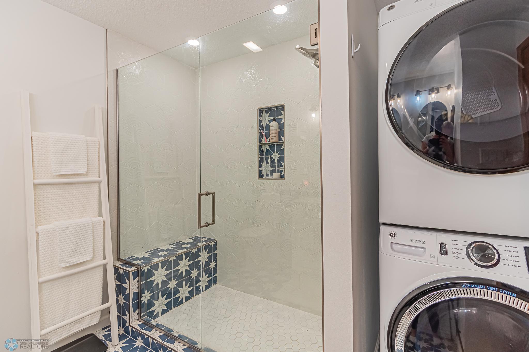 Walk-in tiled shower and staked washer/dryer in primary bathroom