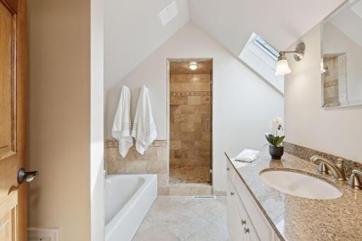 Updated guest bath with tub, separate shower, heated tile floor, vanity, and skylight.