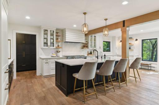 An open-concept gourmet kitchen with gorgeous private views of the land and pond which boasts custom cabinetry, quartz countertops, commercial-grade appliances, stunning beams, and a custom walk-in pantry.