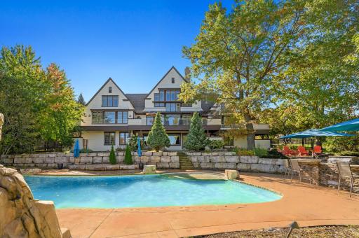 The meticulously landscaped grounds feature outdoor living at its finest, including a custom saltwater pool with a stone waterfall and slide, sport court, lush gardens, and an outdoor kitchen, all enveloped in privacy.