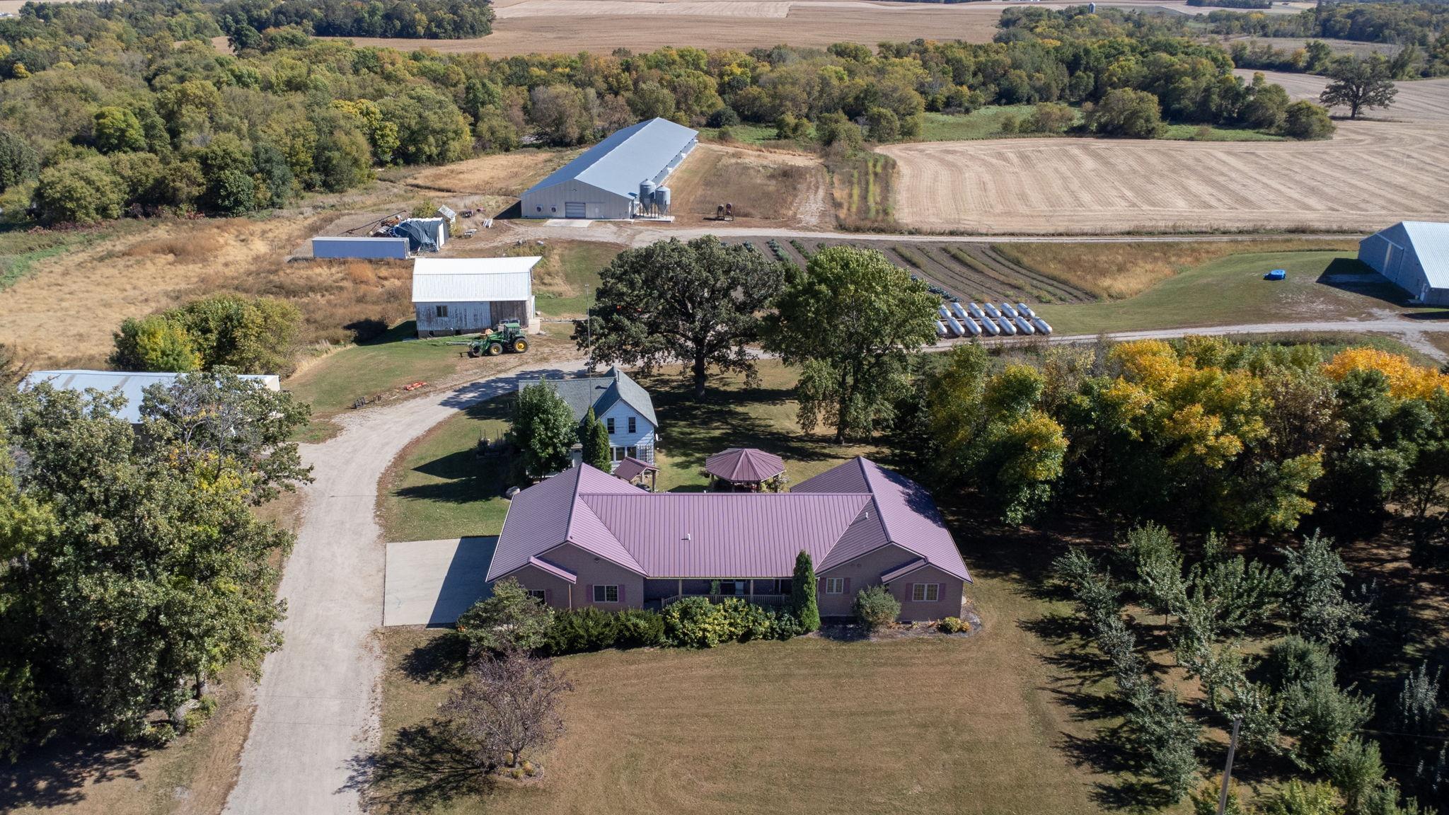 Aerial view of the home, newer barn towards the back, and woods.