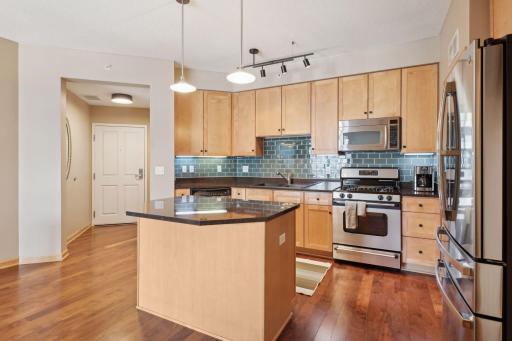 Attractive kitchen with gorgeous maple cabinets, center island, stainless steel appliances, granite countertops, and tile backsplash.