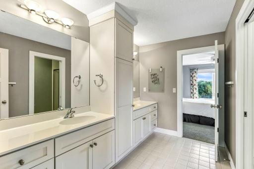Jack & Jill bathroom features dual enameled vanities with additional linen tower and tile flooring