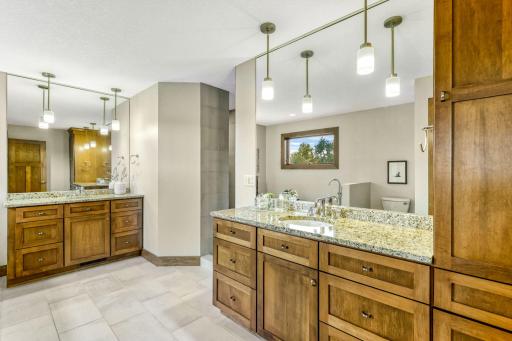 Master bathroom features dual maple vanities with granite countertops, full height mirror with decorative pendant lighting and linen cabinet