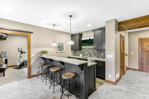 Full bar features rustic alder cabinetry, roll-out storage, granite countertops w/ quartz composite sink, mosaic tile backsplash, travertine flooring and raised countertop to accommodate bar stools