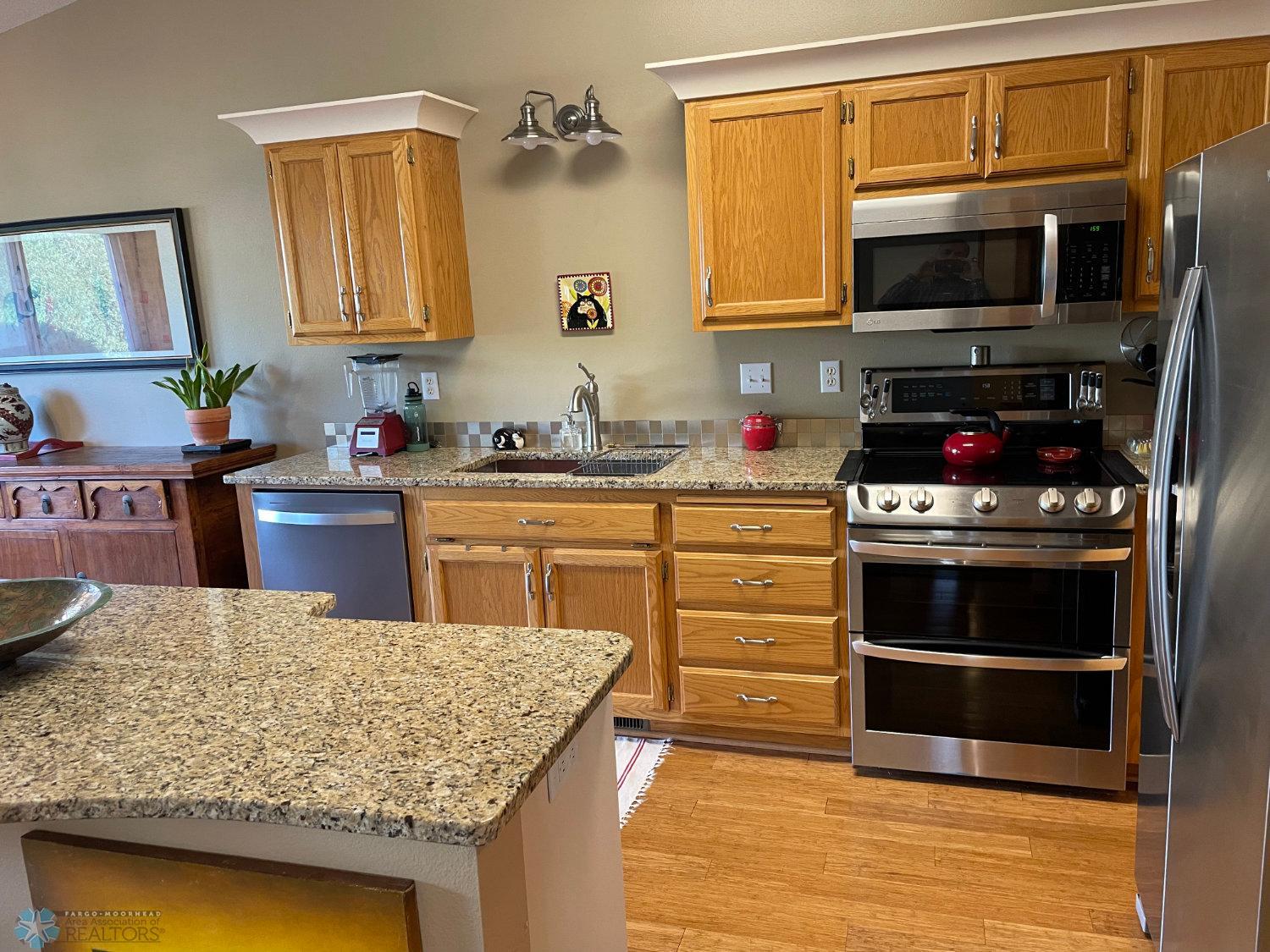 Open remodeled kitchen with granite counters, crown molding on cabinets, and stainless steel appliances. Solid bamboo hardwood floor.