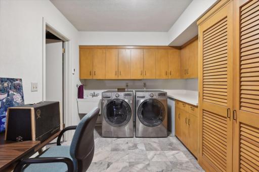 The spacious laundry room has heated tile floors, extensive cabinetry and room for a hobby table