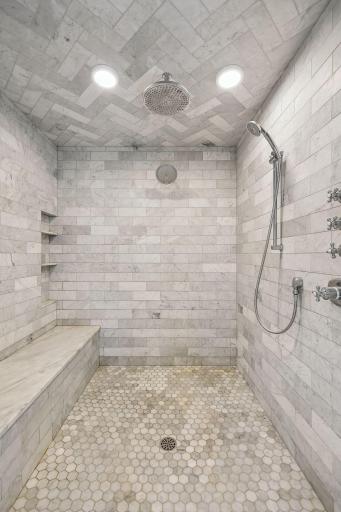 Luxurious marble walk-in shower with long built-in bench and rain shower head.
