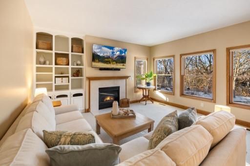 The living room is a sun-drenched retreat, with a wall of Andersen Windows that frame serene views of the tranquil, wooded backyard.