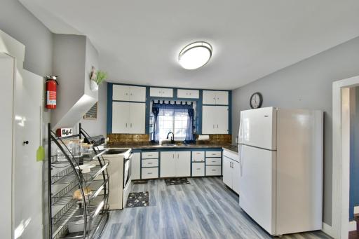 This kitchen features a charming blend of vintage and modern touches, with updated flooring, crisp white appliances, and a pop of color framing the cabinetry. Natural light streams in through the window above the sink, creating a bright and welcoming