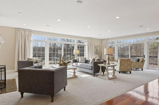 Floor-to-ceiling windows and doors fill the space with natural light and provide views of the natural setting.